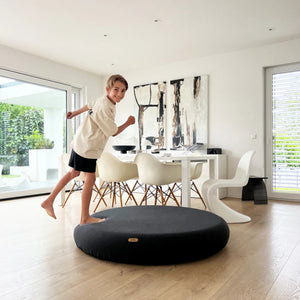 Child balancing and having fun on a large round black indoor cushion in a modern, bright living room - Jupiduu Outdoor Jumpspot