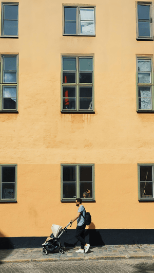 Father pushing stroller with child along yellow building background - premium baby gear from Little Gliders