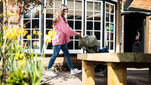 Woman strolling with a Didofy stroller, surrounded by blooming daffodils – award-winning British pushchair designed for comfort and convenience