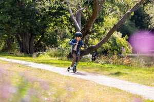 A child zooms down a park pathway on the Micro Sprite kick scooter, dressed in a denim jacket and helmet, enjoying a smooth and exciting ride.