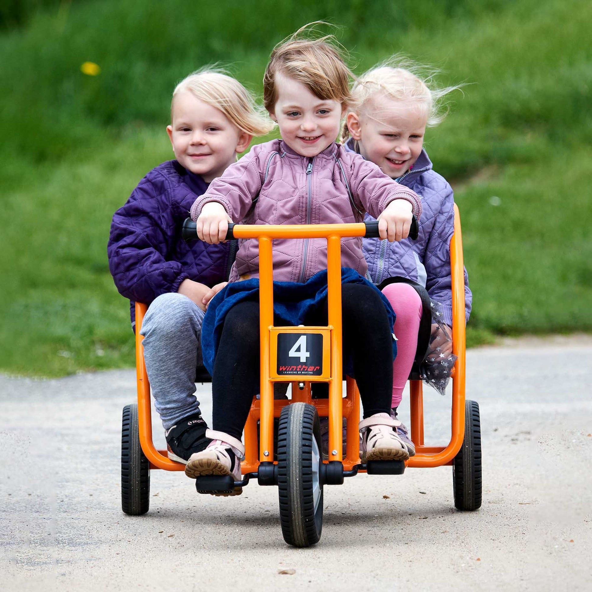 Three children riding a yellow Winther tricycle together, encouraging teamwork and active play – available at Little Gliders.