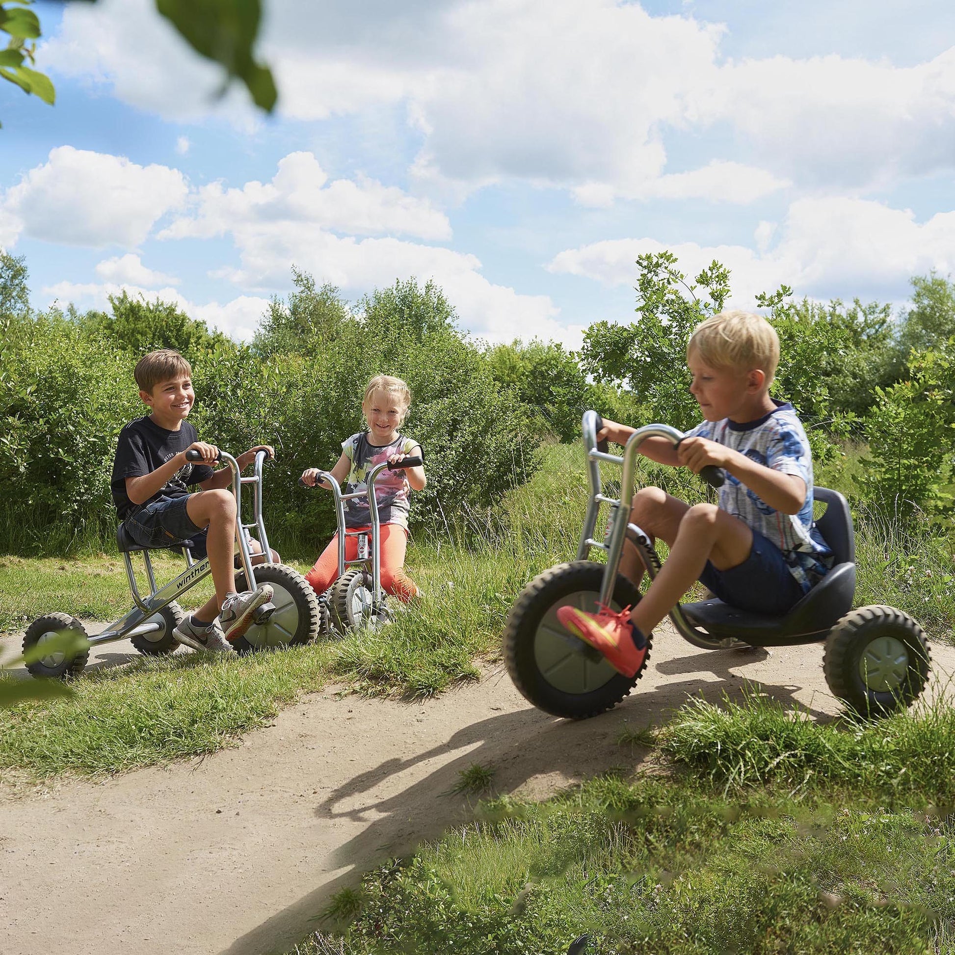 Three children riding Winther Viking off-road trikes on a dirt path, enjoying outdoor adventure and active play – available at Little Gliders.
