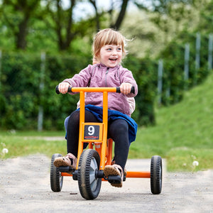 A happy toddler riding a bright orange Winther tricycle, perfect for outdoor activities and motor skill development – available at Little Gliders.
