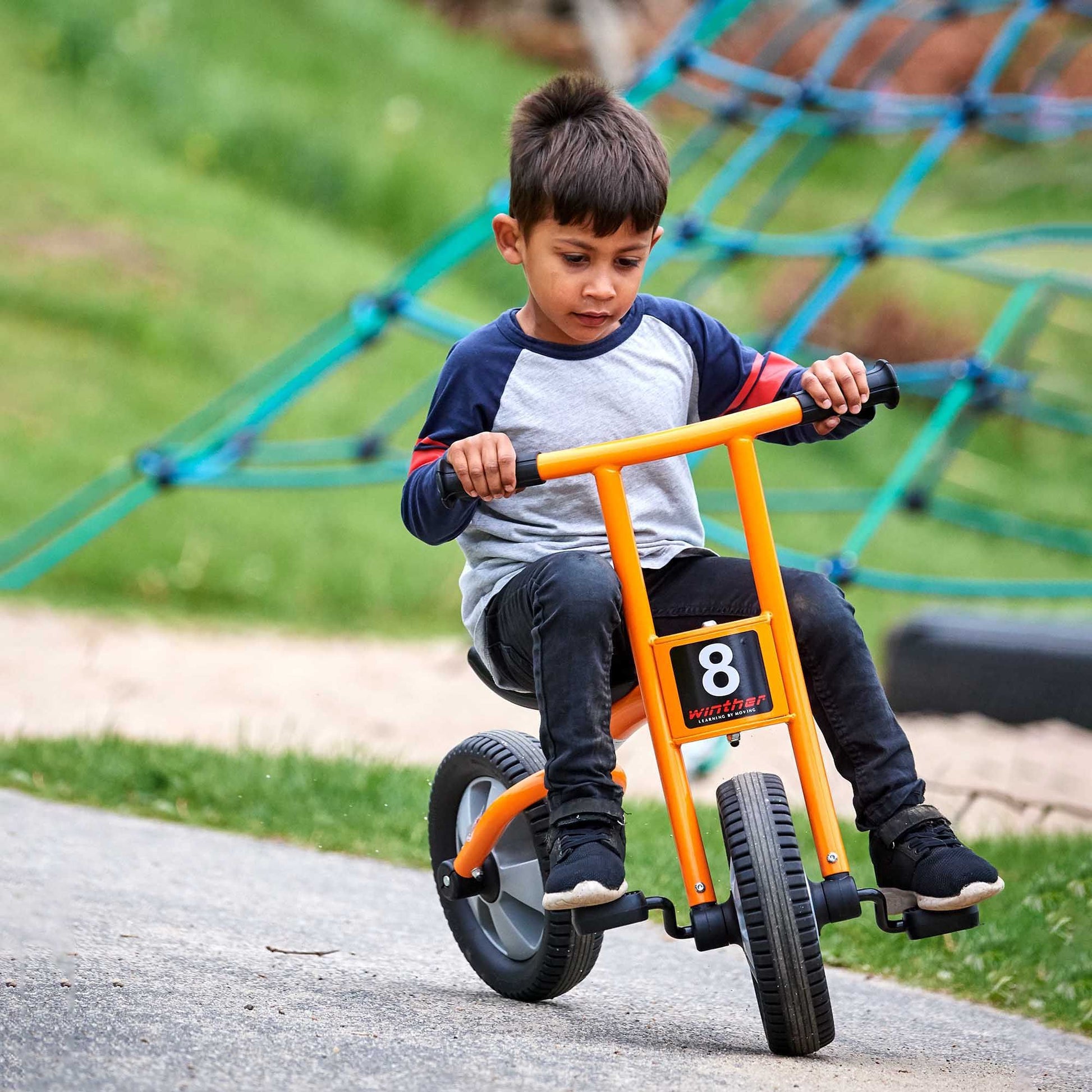 A young boy riding a Winther orange trike outdoors, perfect for developing motor skills and encouraging active play – available at Little Gliders.