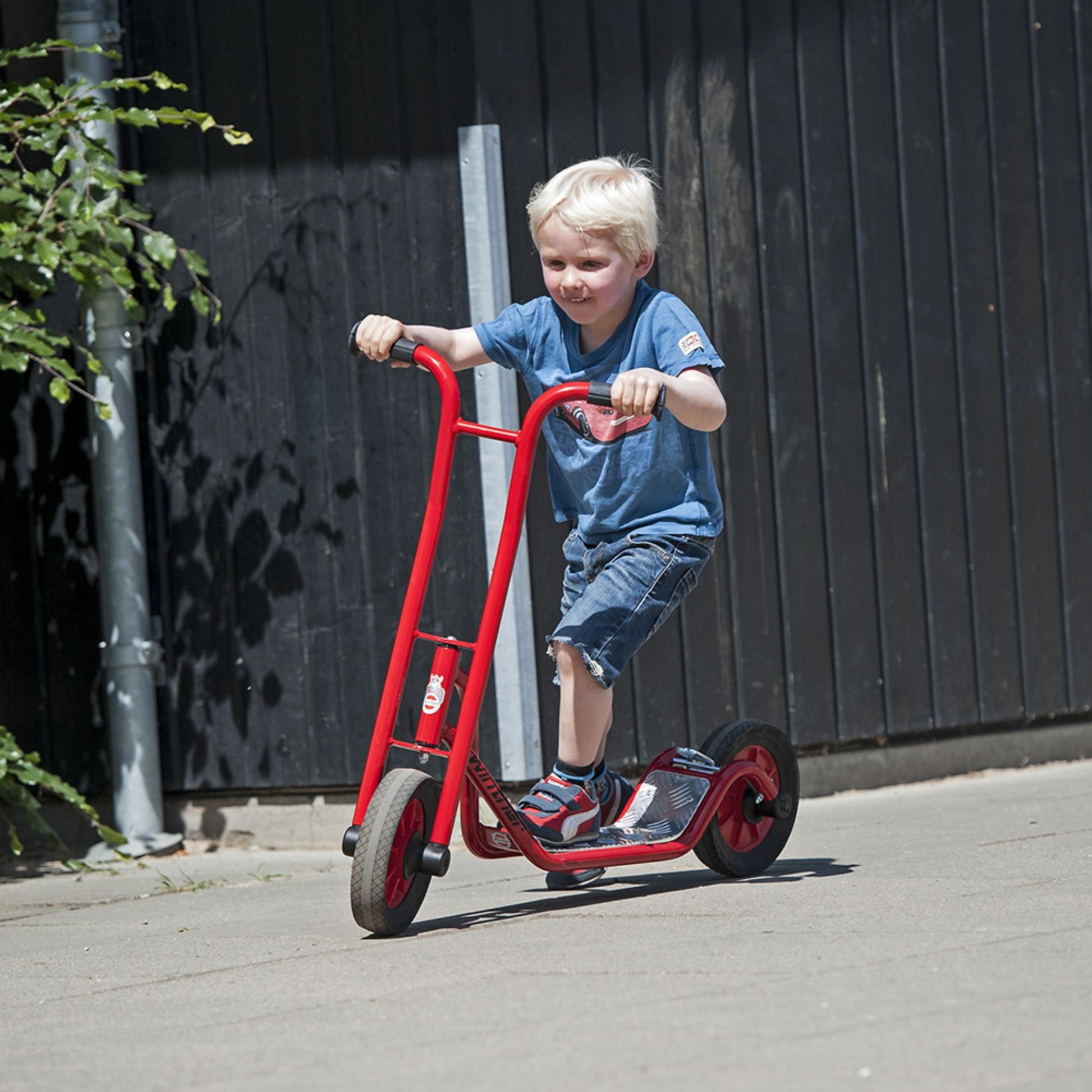 A boy riding a red Winther scooter, enjoying outdoor play and improving balance and coordination – available at Little Gliders.