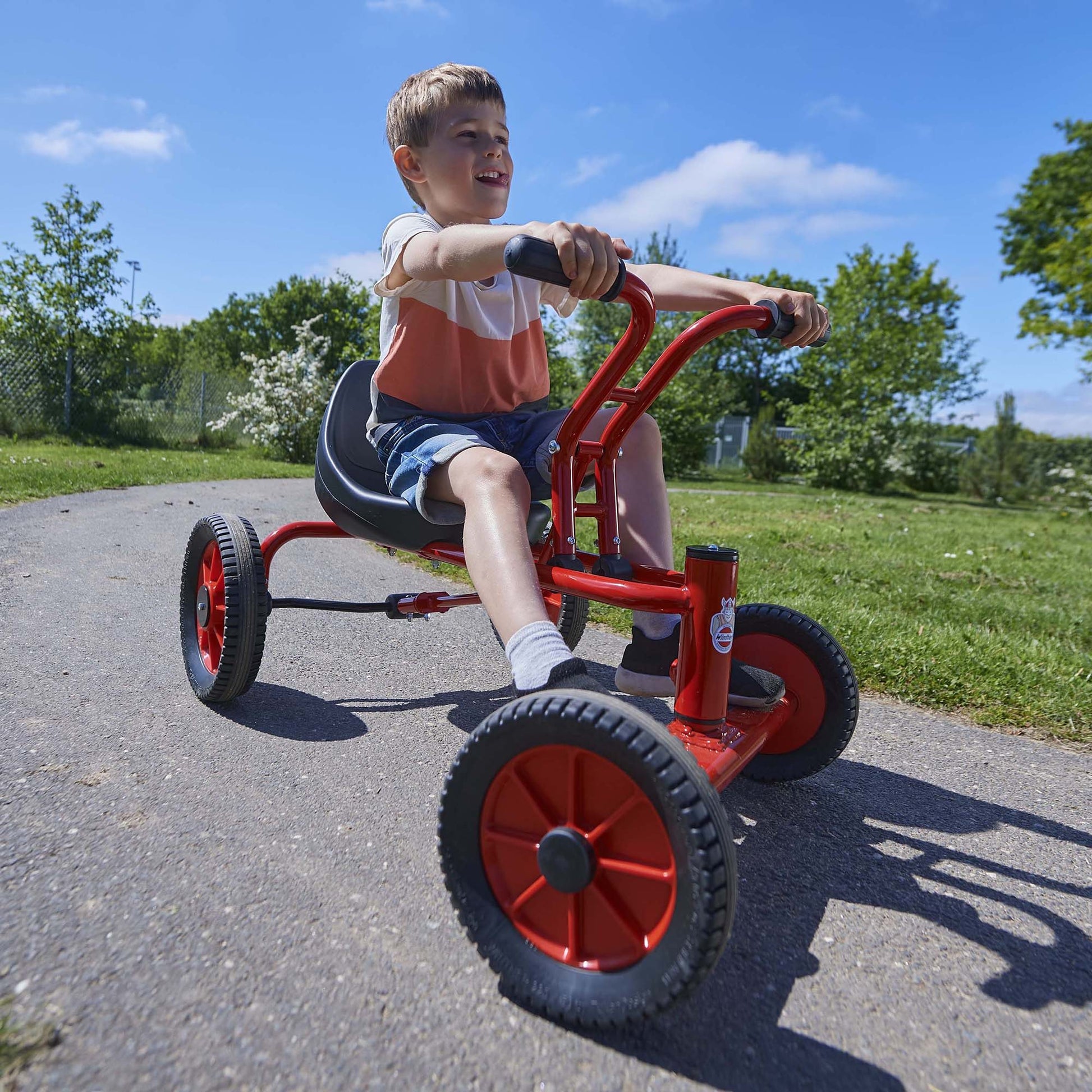 A boy riding a red Winther tricycle outdoors, fostering active play and confidence-building – available at Little Gliders