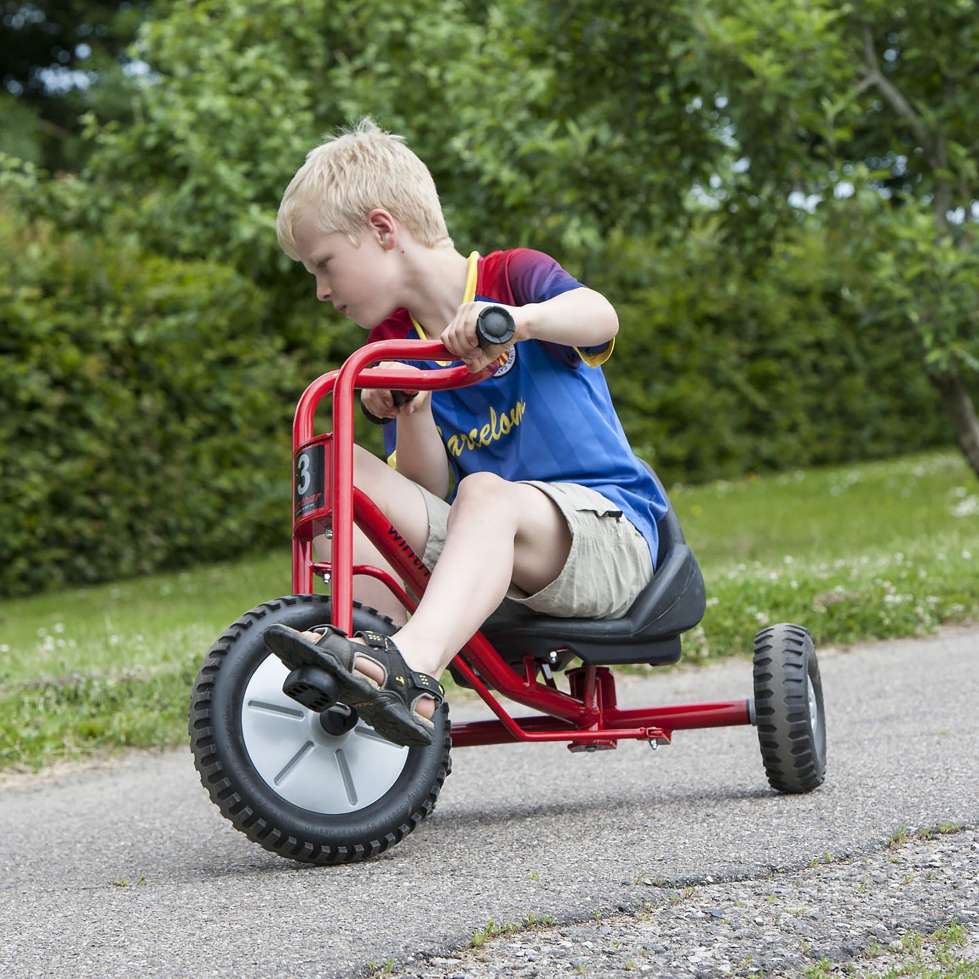 A boy riding a red Winther Viking trike on a sunny day, promoting outdoor activity and confidence-building – available at Little Gliders.