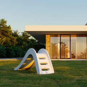 Minimalist white outdoor slide for children placed on a garden lawn, blending beautifully with modern home architecture at sunset.